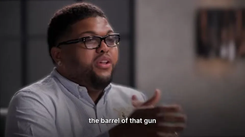Un entrevistado gesticulando con un subtítulo pequeño blanco abajo: «the barrel of that gun»
