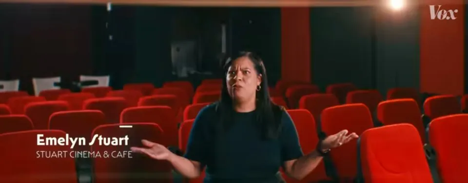 Una mujer en una sala de butacas rojas con el rótulo «Emelyn / Stuart Cinema & Café» abajo a la izquierda