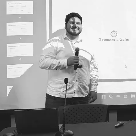 Ponente con un micrófono frente a una pantalla, recortado para dejar fuera la diapositiva