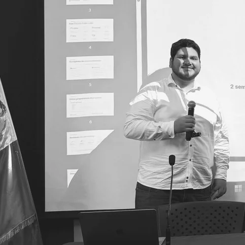 Martín Velasco hablando con un micrófono en un escenario, en blanco y negro